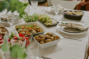 Table set with assorted dishes including roasted potatoes, fresh salad, grapes, bread basket, glassware and plates arranged for meal gathering, no people visible