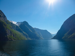 The brilliant sun gleams high above snow-dusted mountainsides plunging into the deep blue...