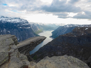 The world-famous Trolltunga rock formation juts out horizontally from a massive cliff, high above...