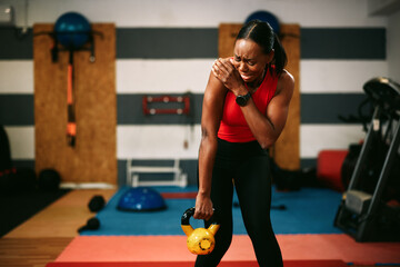 Young female athlete experiencing shoulder pain while lifting kettlebell in gym