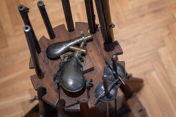 A stand with rapiers, percussion pistols, and powder flasks.
