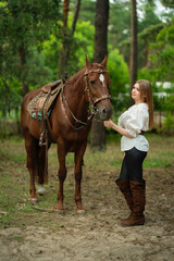 Fototapeta premium Beautiful young woman in stylish white blouse, black pants and high boots with a horse outdoors