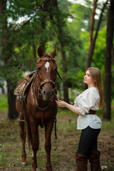 Obraz premium Beautiful young woman in stylish white blouse, black pants and high boots with a horse outdoors
