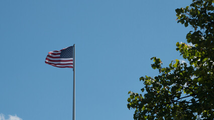 Horizontal photograph of the United States flag waving in the air on a blue sky day.