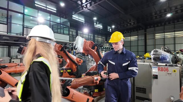 Worker in safety gear overseeing robotic assembly line in modern manufacturing facility