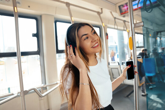 Young woman enjoying music while commuting on public transport with smartphone in hand, vibrant atmosphere and cheerful expression, urban lifestyle concept