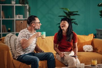 Happy couple relaxing on sofa, drinking coffee and using smartphone