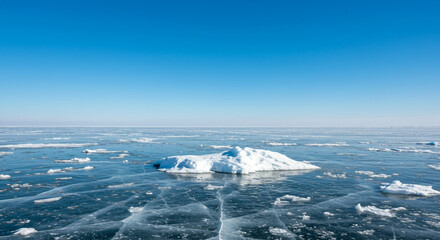 Vast frozen lake stretches under a clear blue sky with scattered ice chunks and a central iceberg formation