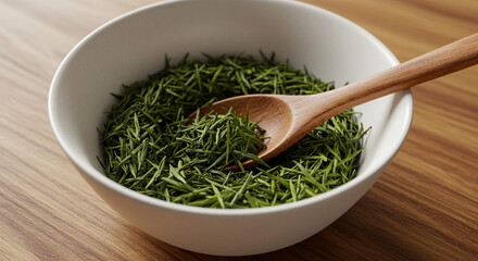 Fresh loose green tea leaves in a white bowl with a wooden spoon ready for brewing a healthy beverage