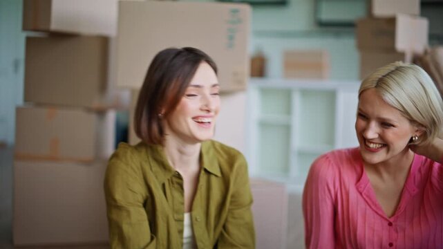 Laughing girls enjoying relocate sitting floor in purchased apartment closeup