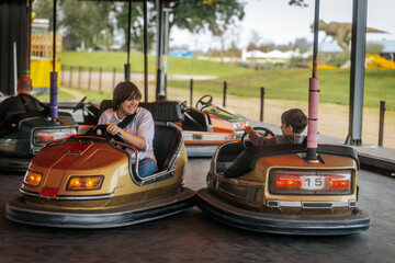 Children and adults enjoy driving bumper cars at an amusement park ride, smiling and laughing in a lively, colorful atmosphere.
