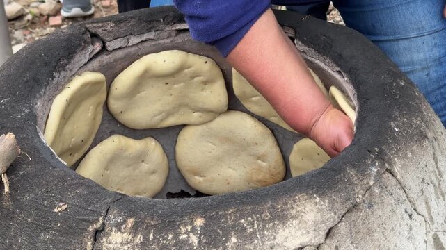 Woman cooking Traditional Tunisian flatbread (Tabouna) in a stone or clay oven called a Tabouna
