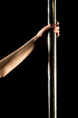 Woman's arm grips a metal pole in dark studio setting