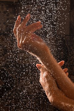 Woman's hands under shower stream with water droplets