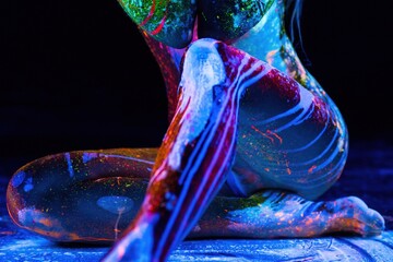 Woman's body covered with fluorescent paint under black light