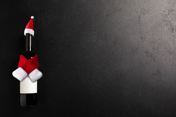 Santa claus hat and scarf on bottle with red wine on black background. Flat lay. Christmas  celebration