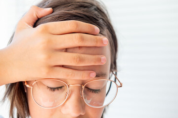 Young teenage child in glasses holding head in pain, pre-teen boy suffering from headache,...