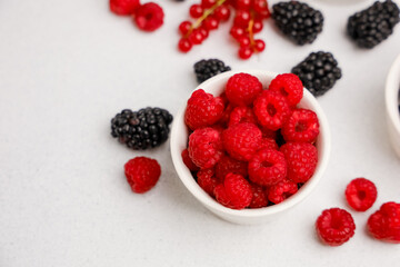 Fresh red raspberries and blackberries arranged in bowls on a light surface