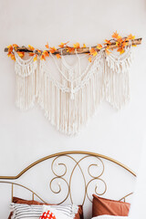 Macrame wall decor with autumn leaves above a bed in a cozy bedroom setting