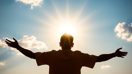 Silhouette of a man with outstretched arms facing the sun against a blue sky with scattered clouds