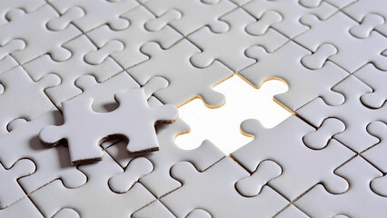 A white puzzle with a missing piece. The final piece is ready to be installed.
