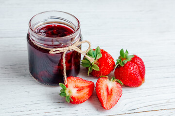 Strawberry jam in a jar with fresh strawberries on a wooden table