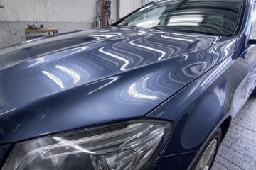 Metallic blue car hood and headlight in a service garage with bright light reflections