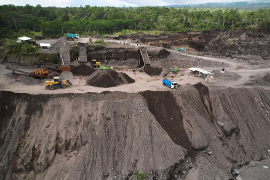 A stone quarry in Indonesia. Large equipment such as bulldozers and dump trucks are working on the site.