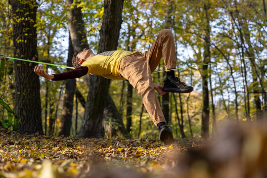 man in yellow t-shirt laying on slackline in autumn park