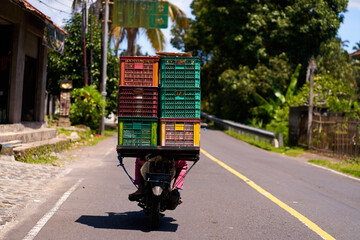People are riding a heavily loaded motorcycle. Asian people are carrying goods for their small local businesses.