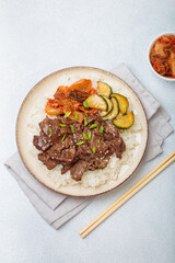 Beef bulgogi bowl dish with rice, roasted meat slices, kimchi and marinated cucumber on white background, traditional dish of Korea