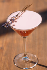 Pink cocktail with lavender sprig on wooden table in sunlight