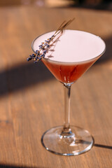 Refreshing pink cocktail garnished with lavender sprig on wooden table