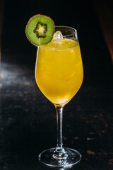 Refreshing yellow cocktail garnished with kiwi slice on dark background