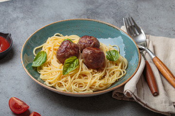 Plate of spaghetti topped with meatballs and basil leaves, accompanied by tomato sauce, fork, spoon, napkin, and tomato slices, healthy home cooking