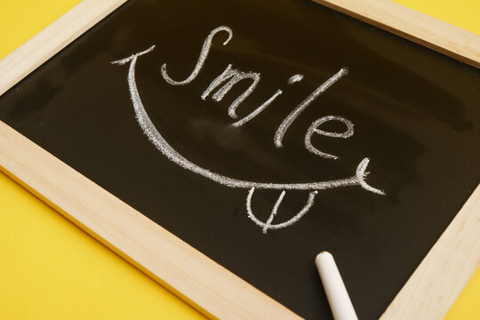 drawn smile and inscription on black chalk board, yellow background