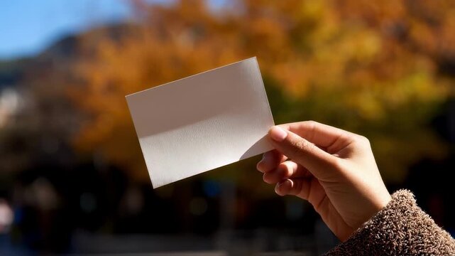 Medium shot of a person examining brightness of a paper sample under natural light with the paper in sharp focus against a defocused backdrop.