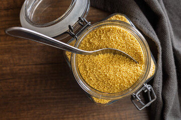 Uncooked couscous in jar on wooden table. Top view.