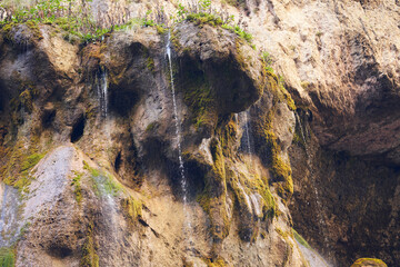 Numerous thin streams of water ooze out of the rock and fall down with a splash of silver threads. A fragment of the main Chegem waterfall.