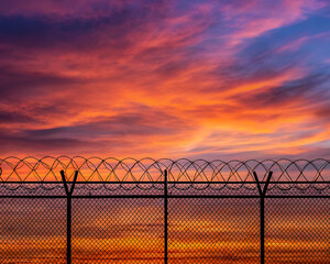 Barbed wire fence against a dramatic fiery sunset sky