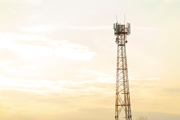 A tall telephone tower rises against a beautifully cloudy sky during a stunning sunset, casting shadows on the ground below