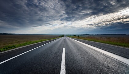 Naklejka premium a long highway stretches into the distance with clear white lines on a freshly paved asphalt surface under a dark sky