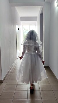 A girl in a white dress and a veil, the image of a scary bride, a zombie,walks around the house, on Halloween