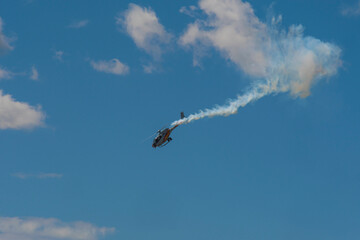 Single helicopter performing a steep aerobatic dive with smoke trail in the sky.