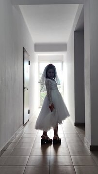 A girl in a white dress and a veil, the image of a scary bride, a zombie,walks around the house, on Halloween