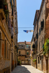 Laundry drying above narrow street in Venice. Colorful clothes hang on lines between rustic Venetian buildings on a quiet stone street, capturing everyday life under the sun.