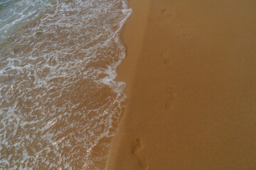 Footprints in the sand on the beach with sea wave, Thailand.