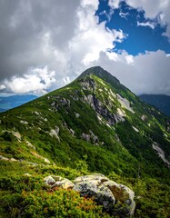 A majestic mountain peak rises amidst a vibrant tapestry of lush green vegetation and dramatic clouds.