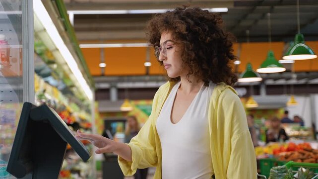 Woman using self checkout kiosk in supermarket