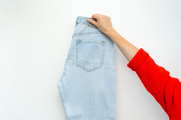 A minimalist studio shot of a hand holding up a single pair of light blue jeans on a clean white background, highlighting fashion and product.
